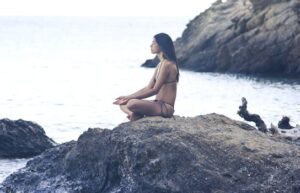 A serene scene of a woman meditating on rocks by the sea, embodying relaxation and tranquility.