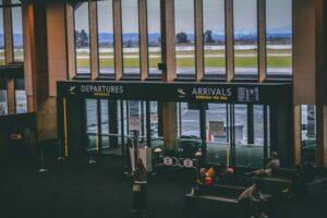 Busy airport terminal area with people, featuring departures and arrivals signs.