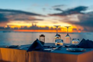 Elegant dinner setup by the ocean during a stunning sunset, creating a romantic ambiance.