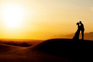 Silhouette of a couple kissing on a dune during a romantic sunset, ideal for wedding themes.
